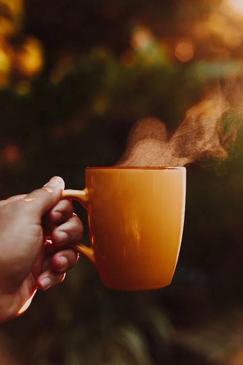 a person is holding a steaming orange mug