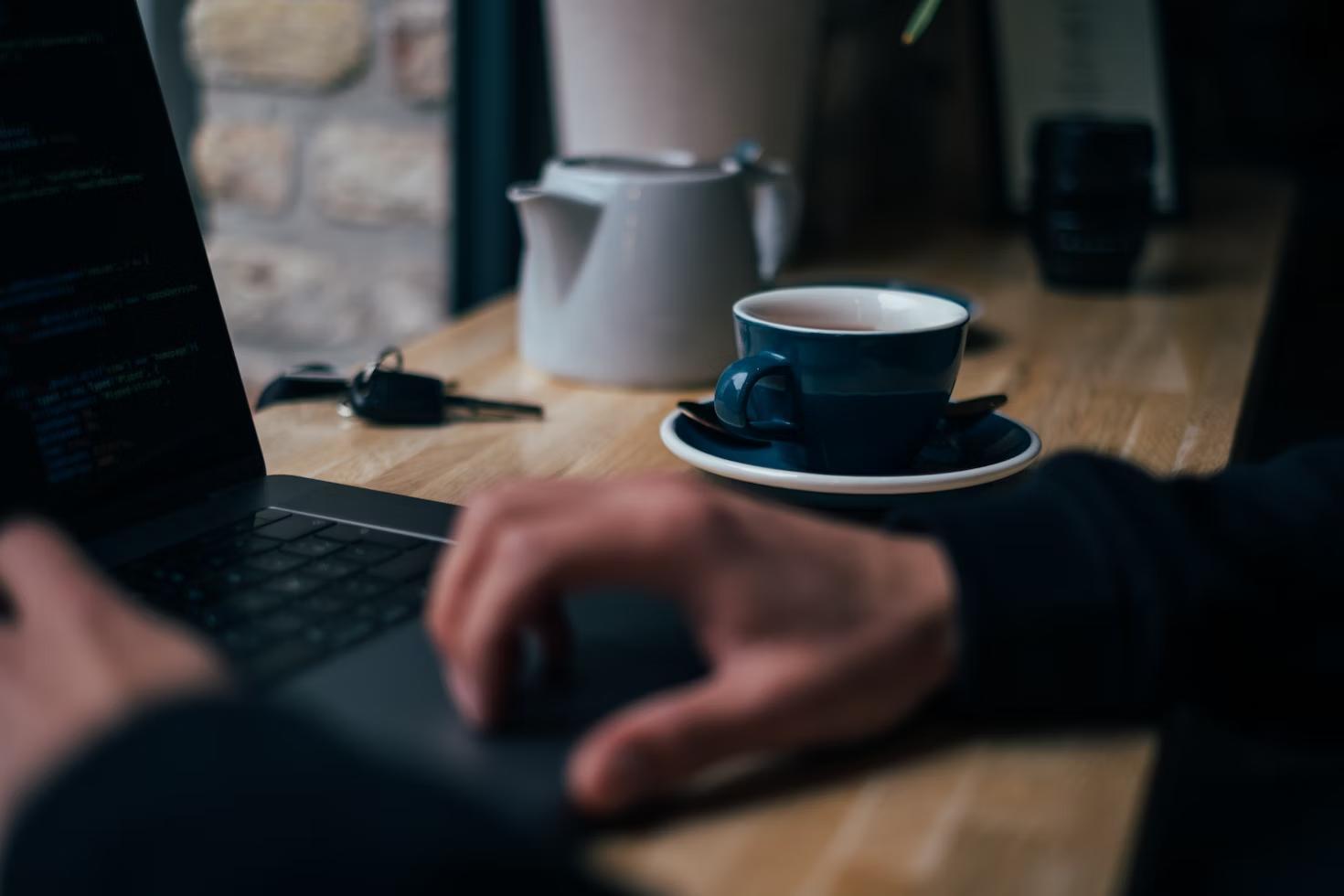 a person working on a laptop at a wooden counter with a cup of tea