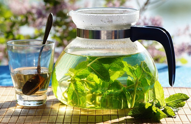 Glass teapot filled with fresh mint tea beside a glass cup and spoon