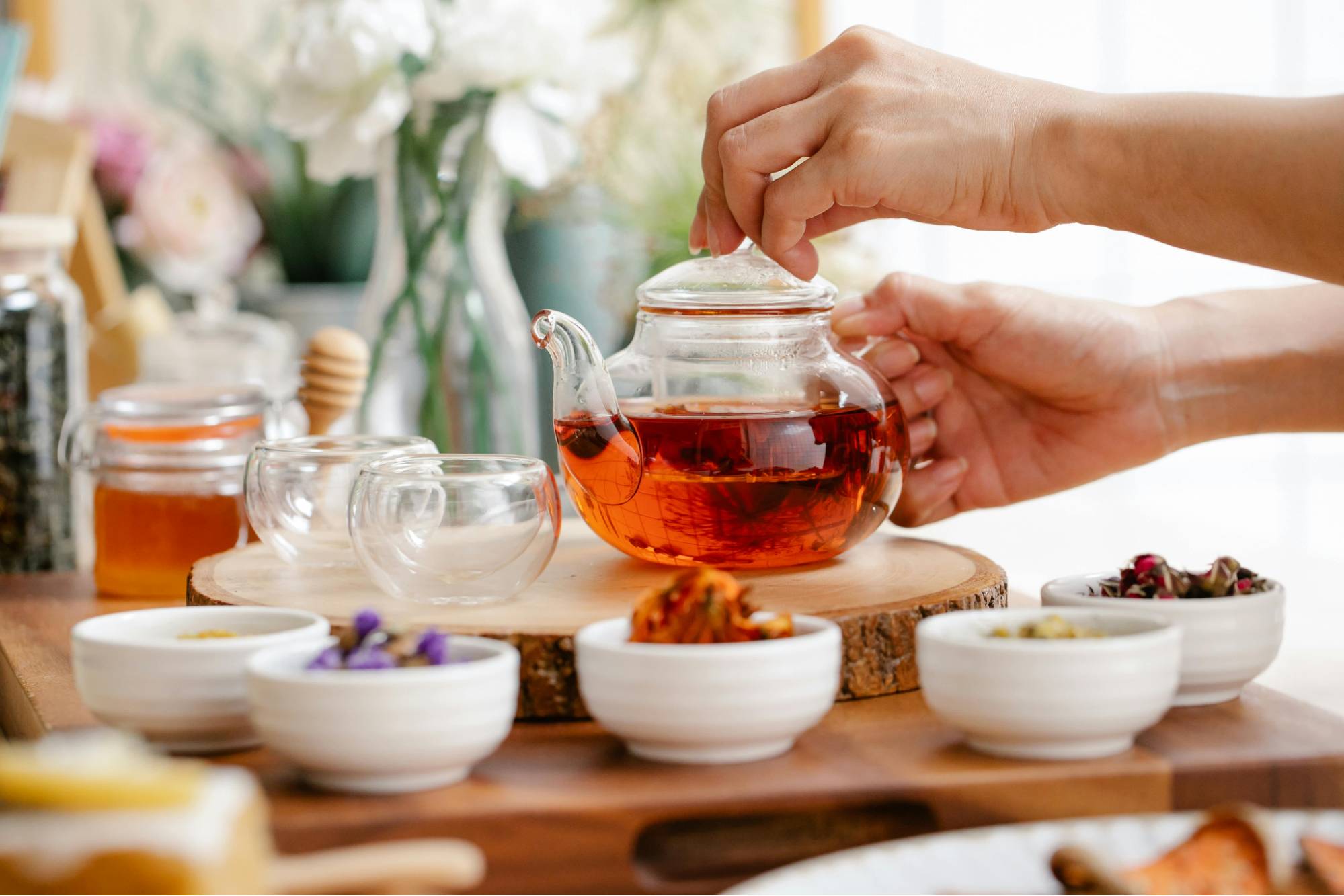 Hands adjusting a clear teapot filled with amber tea