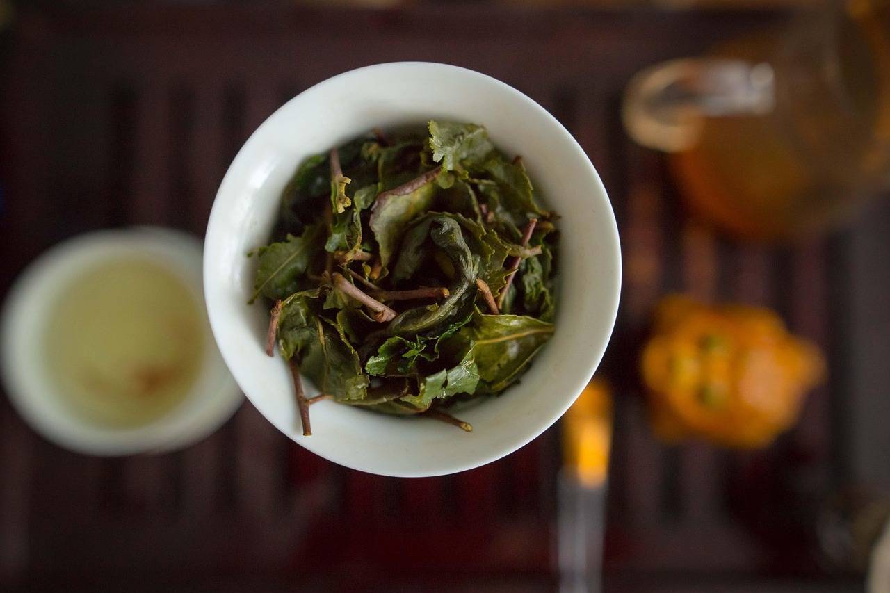 Loose Green tea leaves in a white cup on a wooden table.
