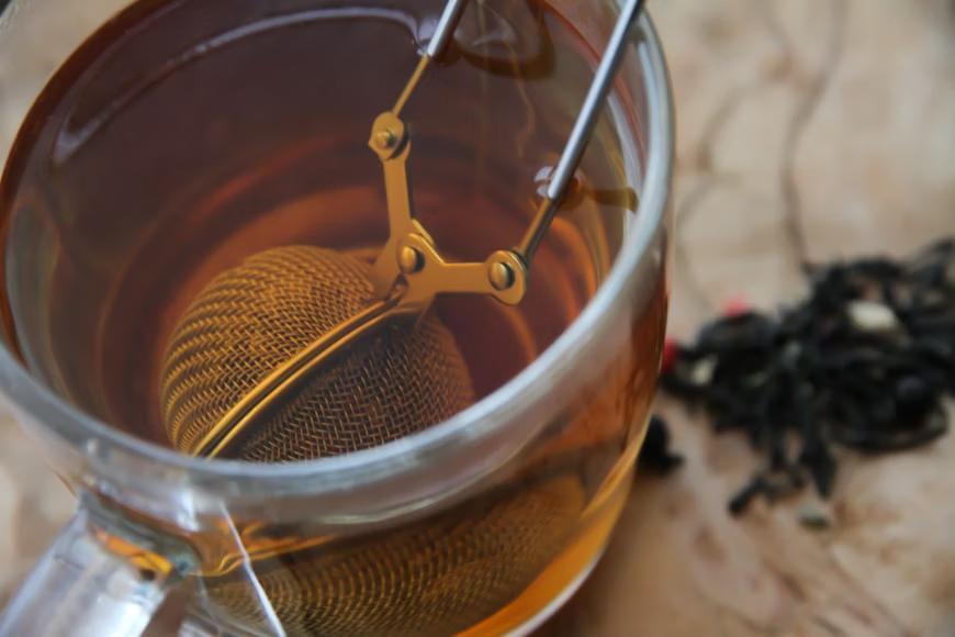Tea infuser steeping in a clear mug of amber-colored tea.