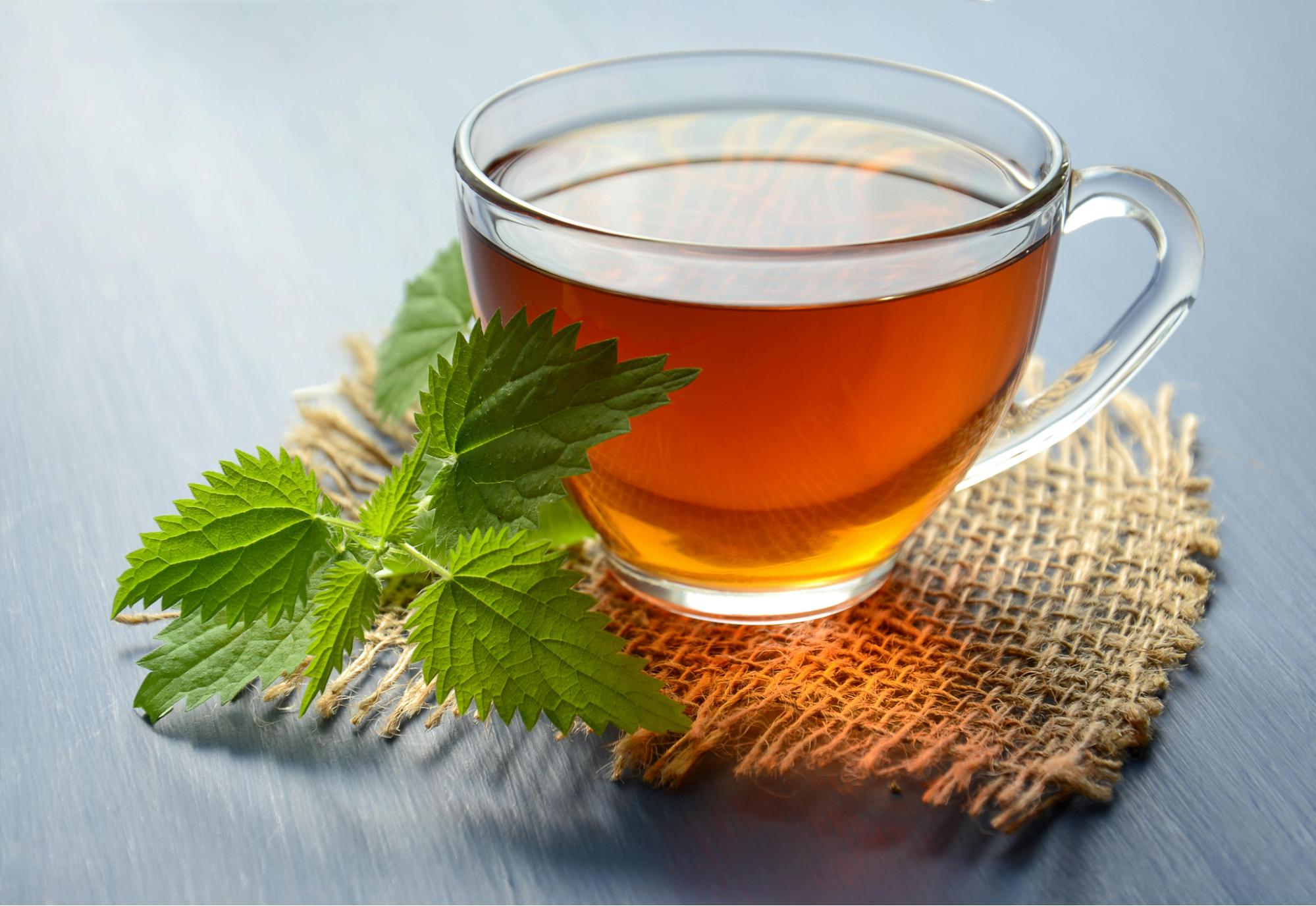 Clear glass cup of herbal tea with fresh green leaves on a burlap coaster