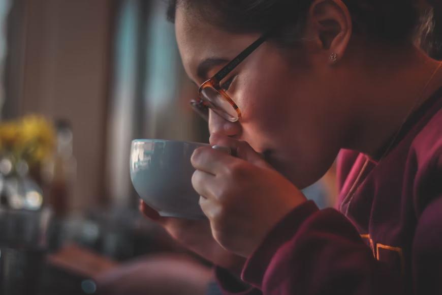 Woman with glasses sipping tea from a white mug.