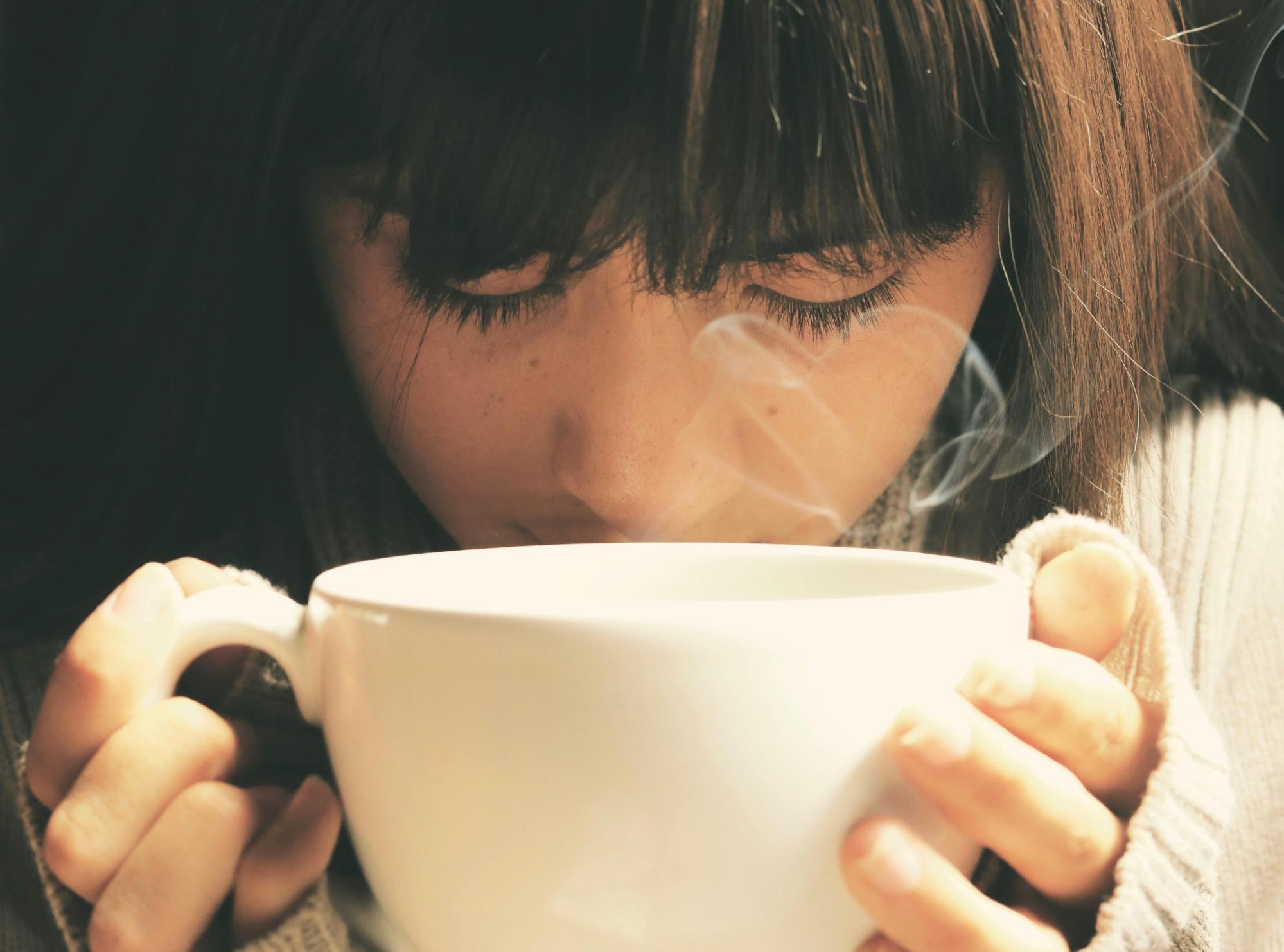 Person holding a steaming mug, eyes closed