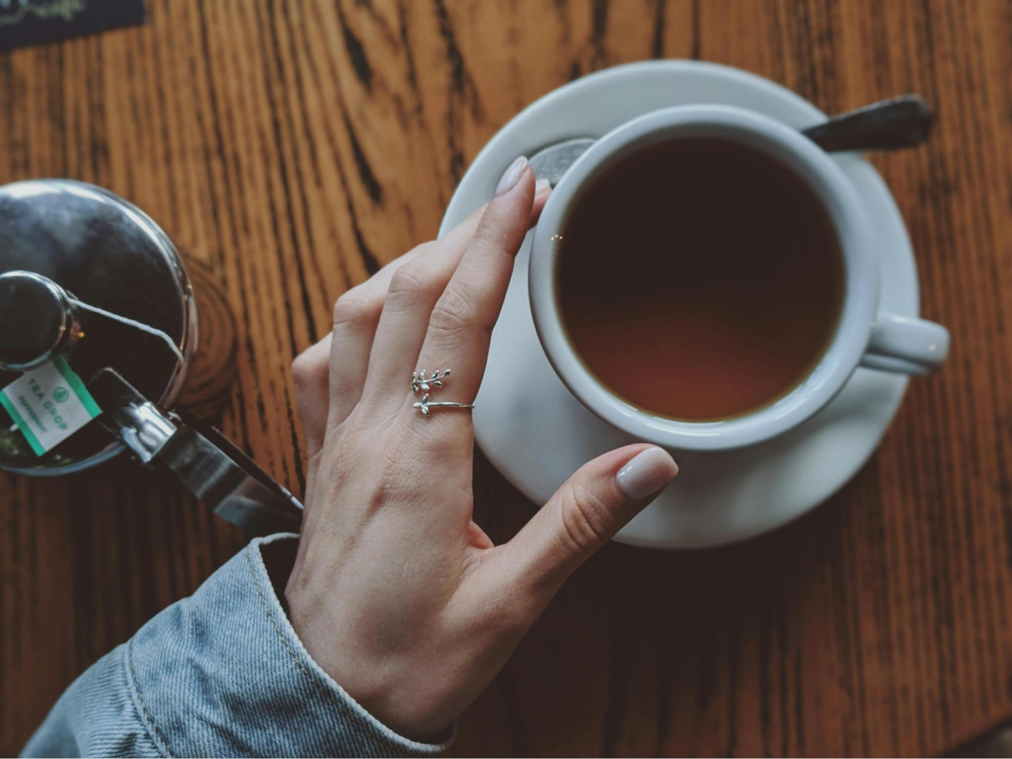 Hand resting next to a cup of tea on a wooden table.