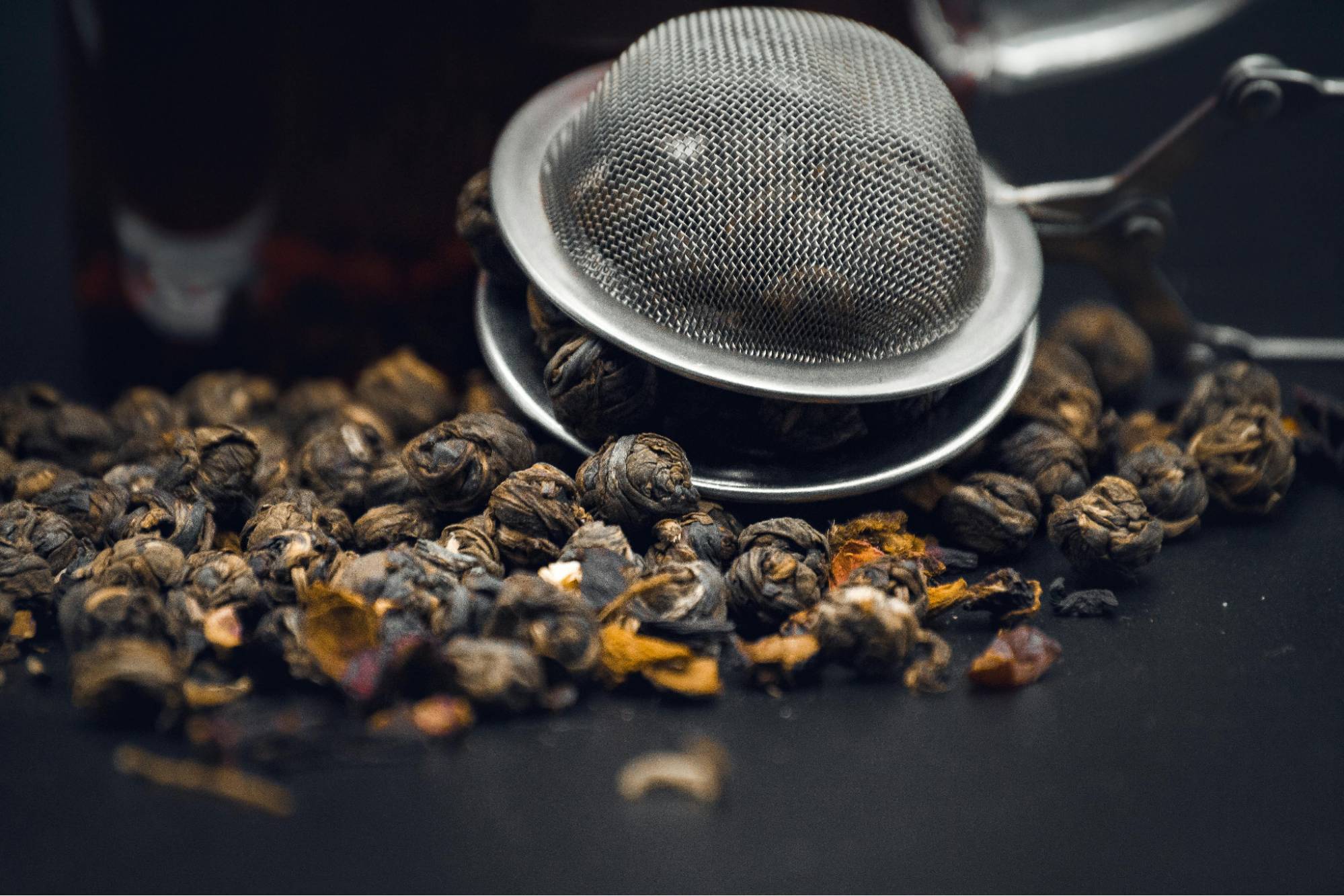 A tea infuser filled with dark, rolled tea leaves