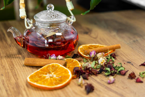 Glass teapot with herbal tea, dried orange slices, cinnamon, and flowers