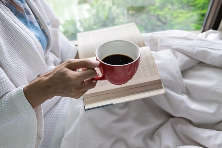 Person holding a cup of tea while reading in bed