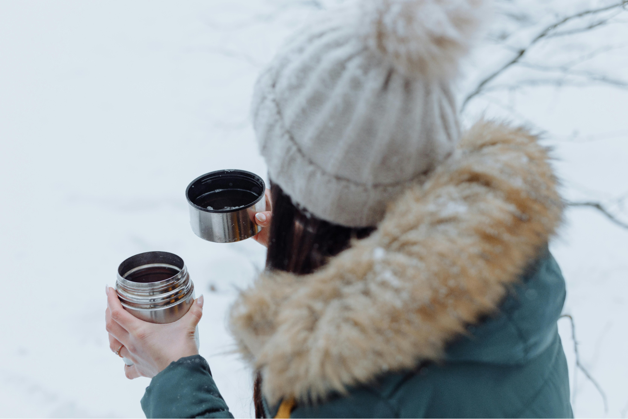 A person is holding a thermos and pouring tea into the cup