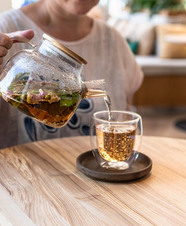 Person pouring herbal tea from a glass teapot