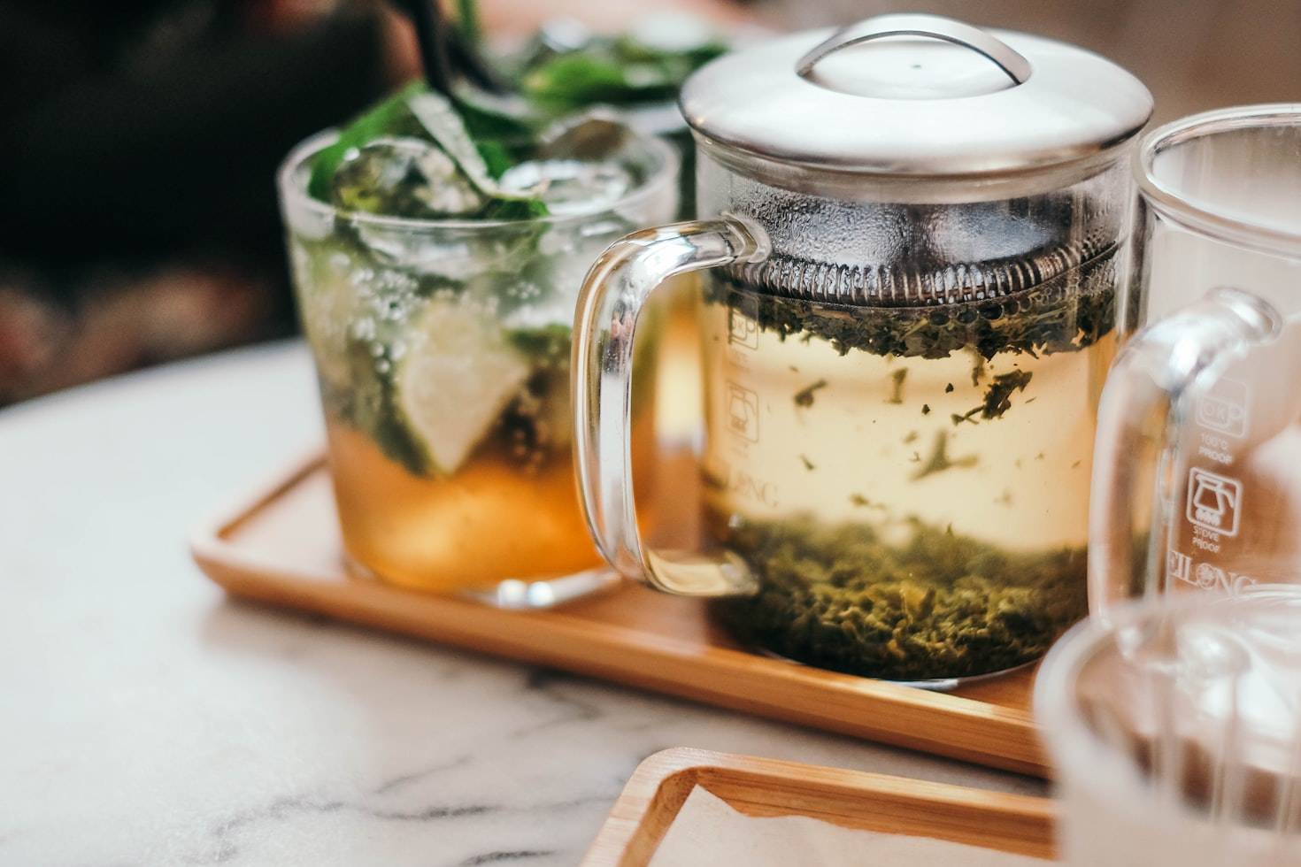 Green tea brewing in a glass teapot on a tray