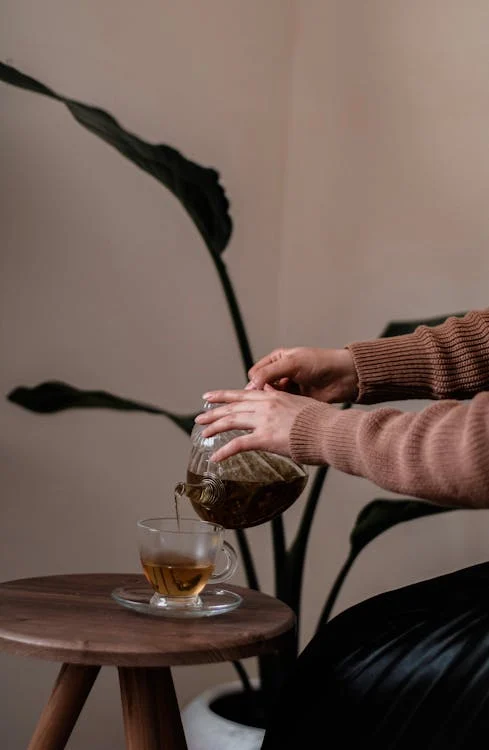 Woman pouring tea from a teapot into a glass cup