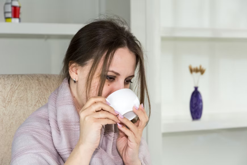A woman sips tea from a white teacup