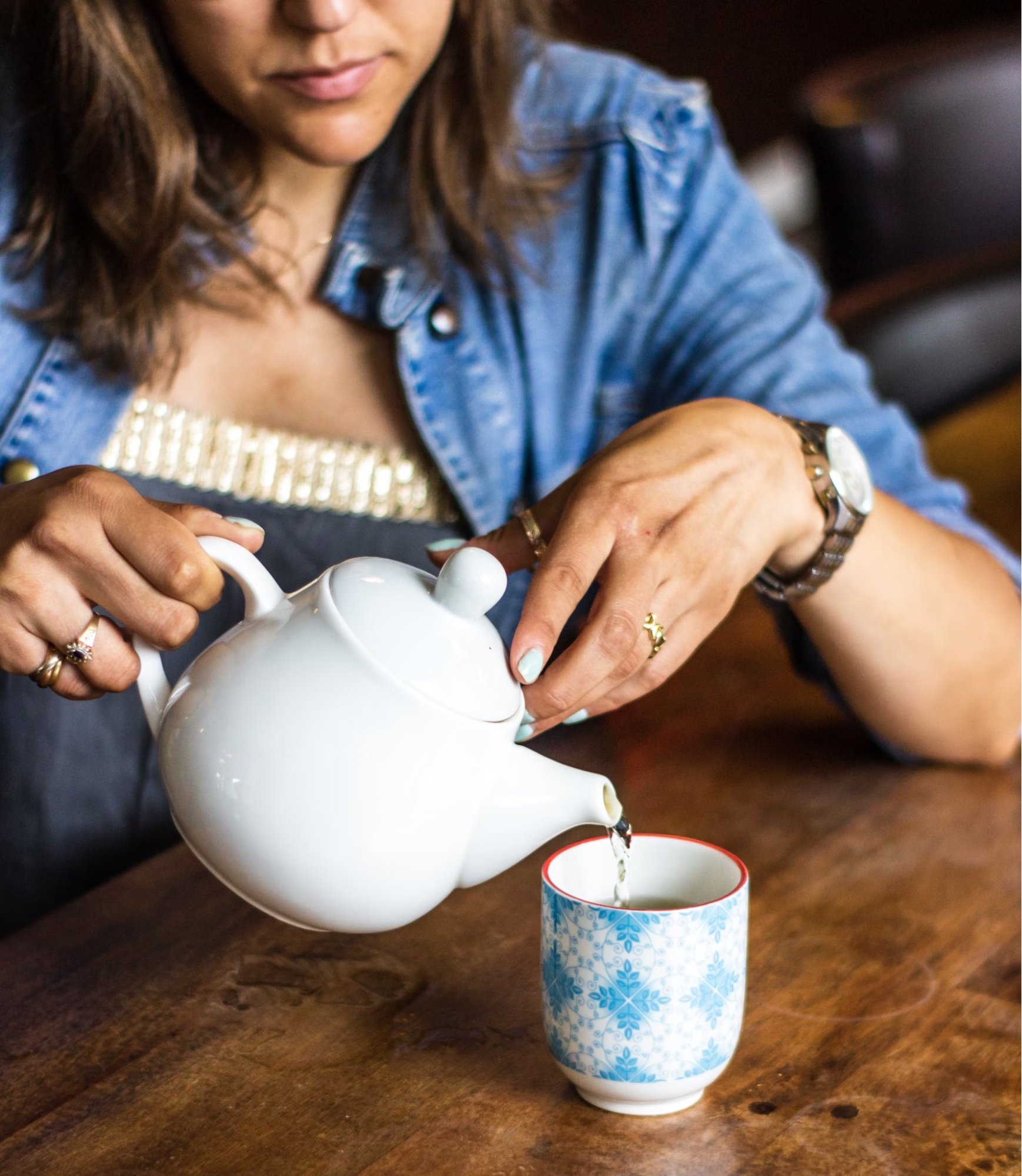Women pouring tea on a cup from a white kettle